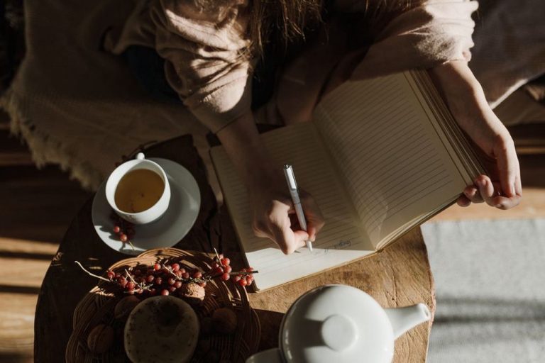 person recording food test results in a notebook with a warm drink nearby