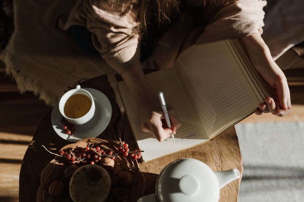 person recording food test results in a notebook with a warm drink nearby