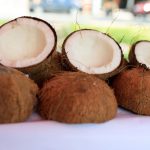 Two cans of full-fat coconut milk on a rustic table next to a halved fresh coconut
