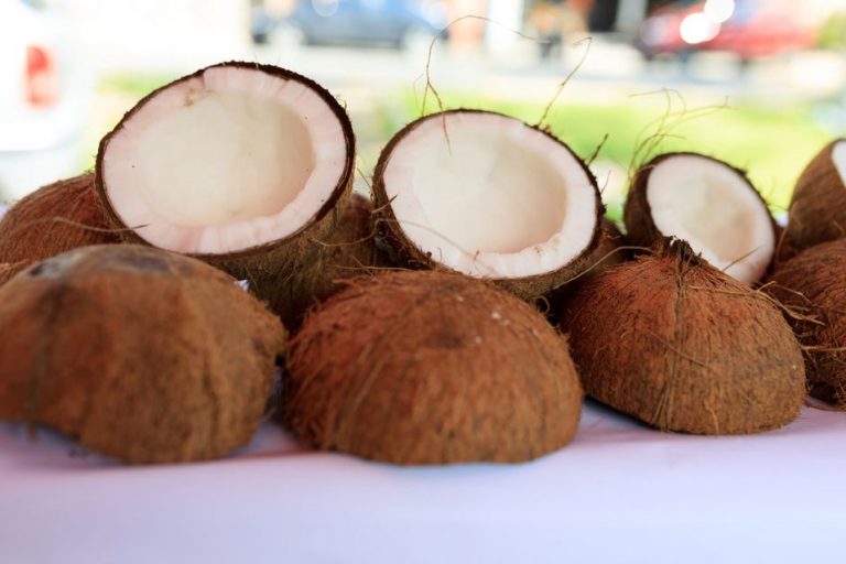 Two cans of full-fat coconut milk on a rustic table next to a halved fresh coconut