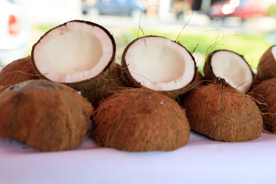 Two cans of full-fat coconut milk on a rustic table next to a halved fresh coconut