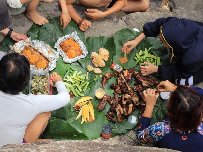 two women eating a colorful salad and grilled meat on a wooden table in a garden
