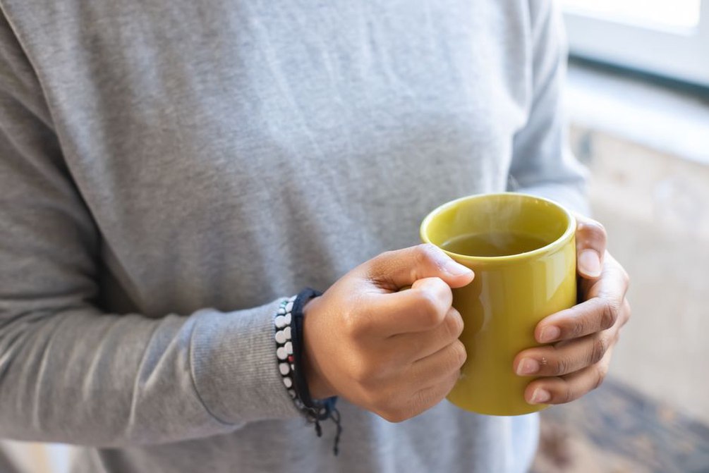 hands cupping a ceramic mug of broth on a rainy windowsill