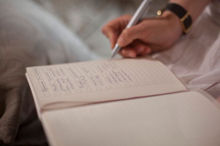 A hand recording daily meals and bloating scores in a paper journal