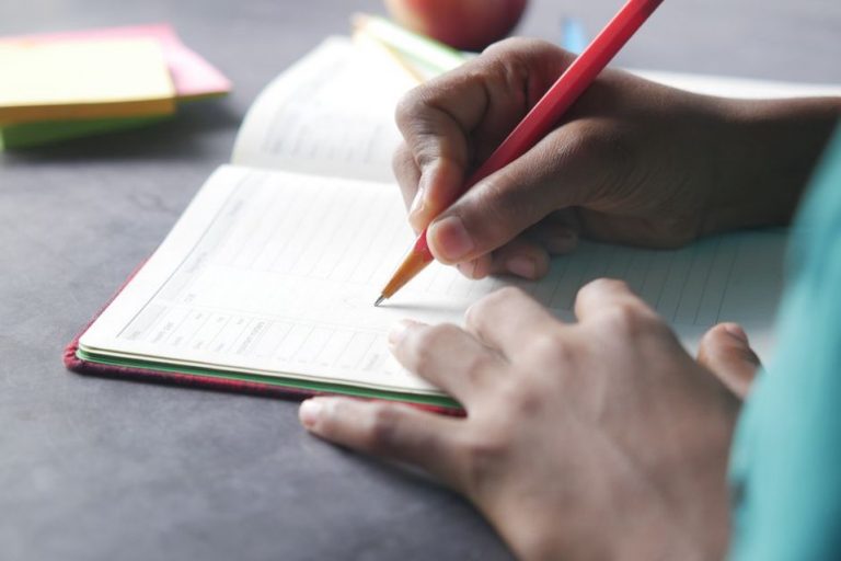 handwritten meal log on a wooden table next to a bowl of fresh greens