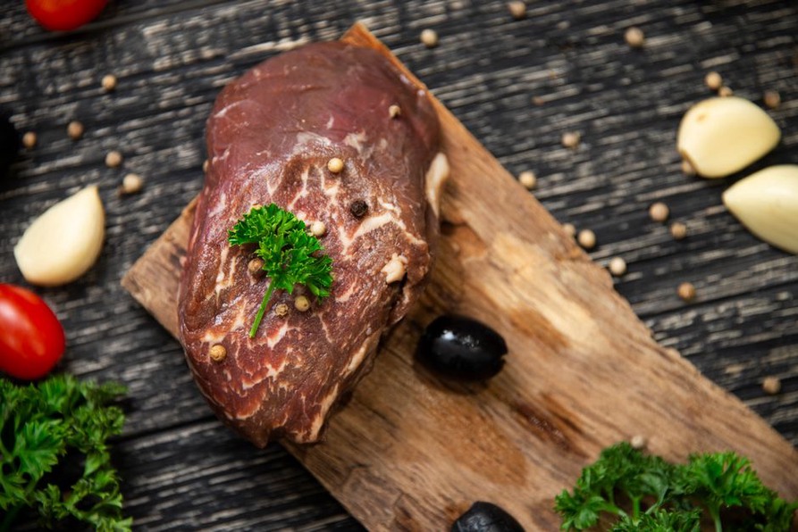 fresh beef liver next to rosemary and thyme on a cutting board