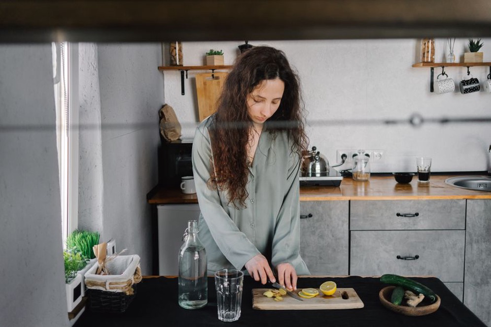 hands holding a glass of water near a cutting board with carrots and leafy greens