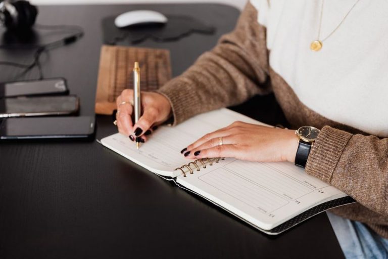 A person logs meals and symptoms in a paper journal next to a plate of fresh vegetables