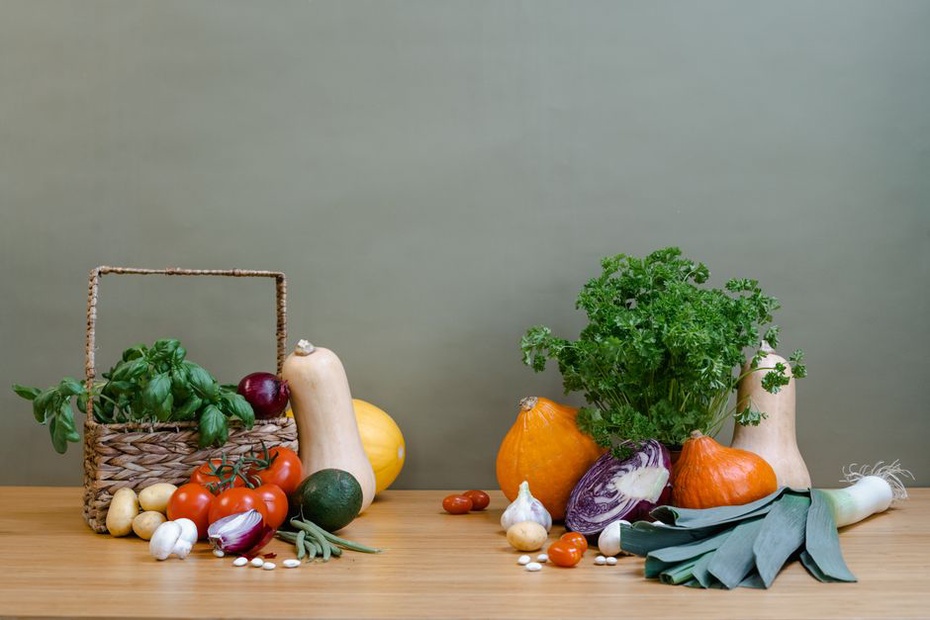 a variety of fresh vegetables, herbs, and fish arranged on a rustic kitchen counter