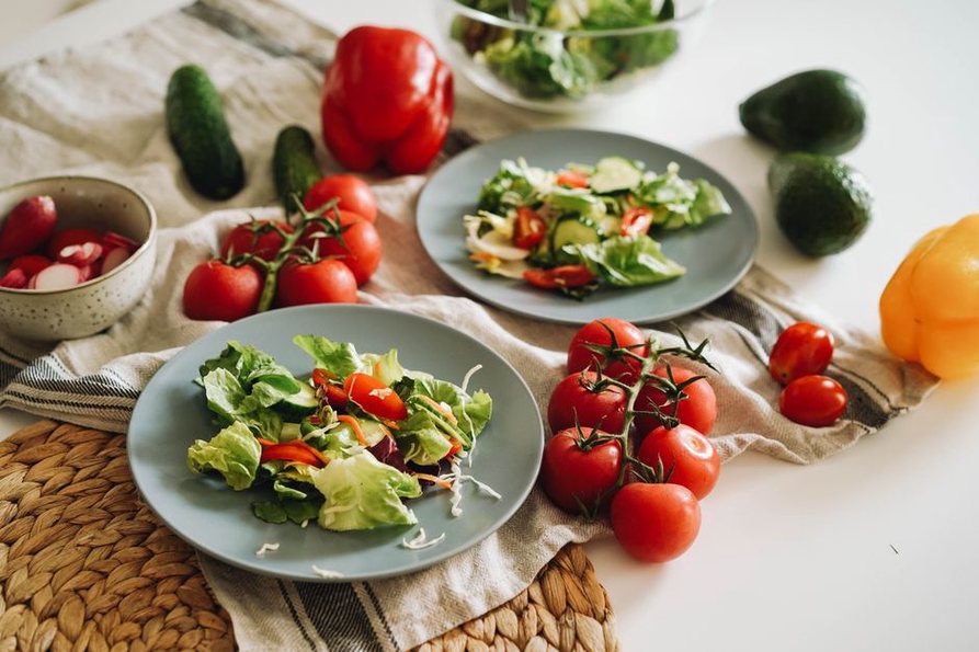 A plate of mixed greens topped with sliced avocado and cucumber, served with a side of olive oil