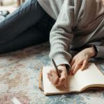 Someone writing in a food diary with a pen and notebook