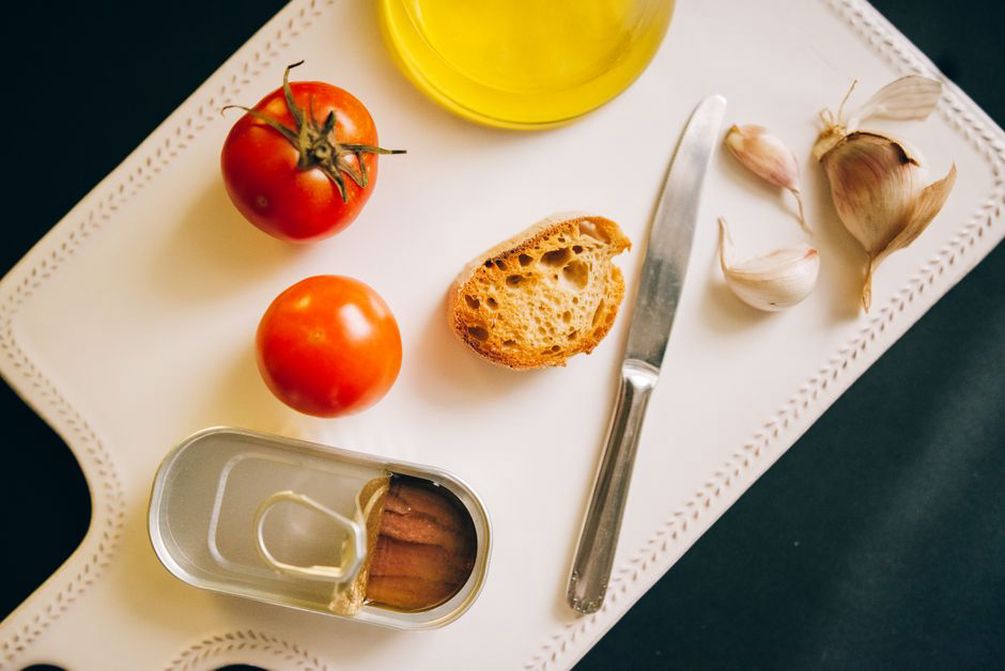 An open tin of sardines beside lunch vegetables